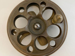 A brass side-mount reel. Large holes are cut through the sides to allow air circulation to help dry the silk lines used at the time.