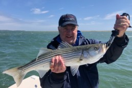 Jim Schottenham standing on a boat, holding a striped bass.