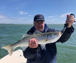 Jim Schottenham standing on a boat, holding a striped bass.