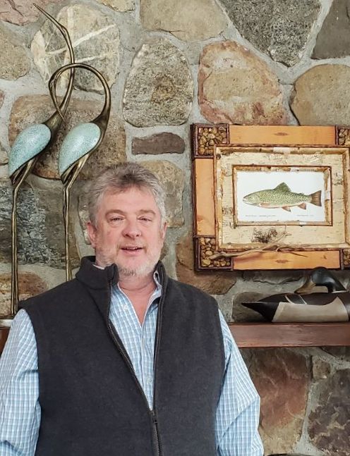 Jim Schottenham standing in front of a stone fireplace.