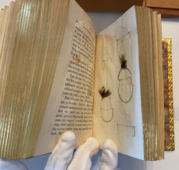 A copy of The Art of Angling Improved, in All Its Parts, Especially Fly-Fishing with two real flies attached to a page.