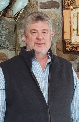 Curator Jim Schottenham stands in front of a stone fireplace.