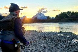 The sun is on the edge of the mountain-studded horizon as Paul Bruun, dressed for cool weather, looks out over a stream.