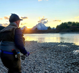 The sun is on the edge of the mountain-studded horizon as Paul Bruun, dressed for cool weather, looks out over a stream.