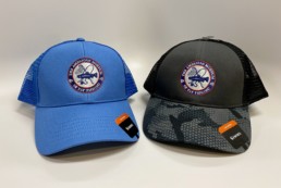 Two trucker hats, one blue and one camo, with embroidered AMFF color logo.