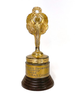 A golden trophy depicting a winged woman holding a laurel wreath over her head. On the label the words trophy, 1939, and fly and bait champion can be seen.
