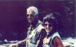 Lee and Joan Wulff turn to smile at the camera as they fly fish on a river.