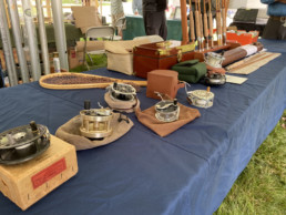 An assortment of antique tackling items are laid out on a table, including reels, a net, and some rods.