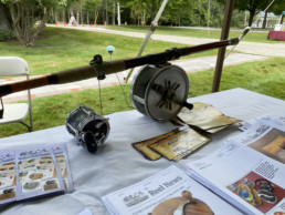 A rod equipped with a large trolling reel sits on the table display of the Old Reel Collectors Association alongside copies of their newsletter.
