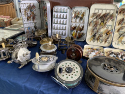 A display of antique reels and metal fly boxes containing salmon flies.