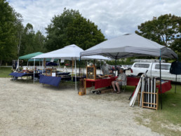 Three pop-up tents sit side-by-side-by-side. A wide variety of fishing goods are arranged under all of them.