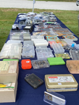 An array of fly boxes, flies, and fishing lines laid out on a table.