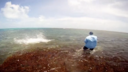 A screenshot of a man fishing in saltwater; there is a large splash subsiding to his left.