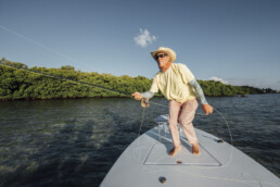 Andy Mill, slightly crouched as he stands on a boat, makes a fly cast.