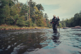 Rachel Finn wades a stream, rod in one hand and wading staff in the other.