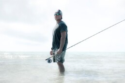 Jose Wejebe stands shin deep in the surf, holding a fly-fishing rod in his left hand and gazing into the distance.